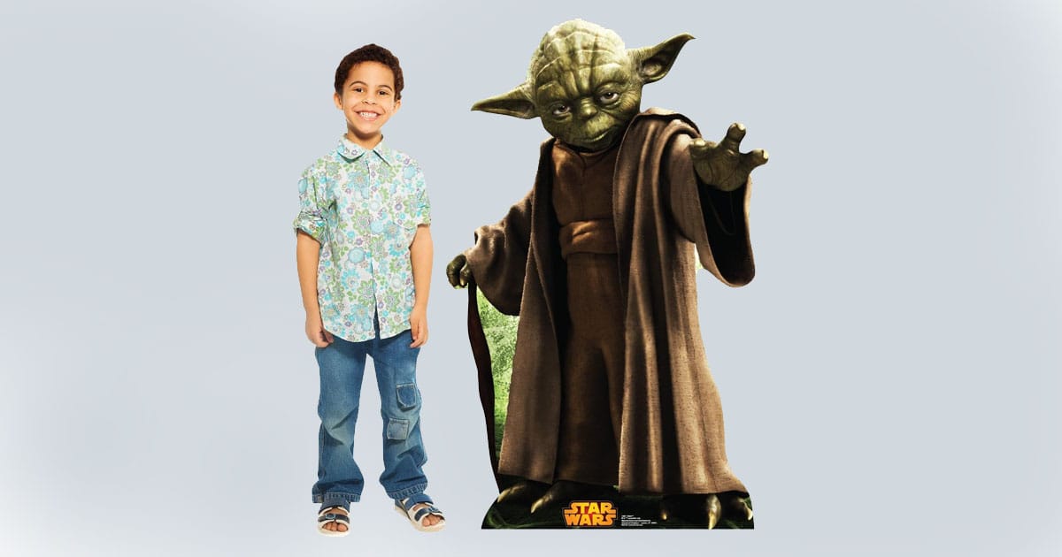 Life-size cardboard cutout of Yoda from Star Wars standing beside a smiling child, showing scale and vibrant character detail.