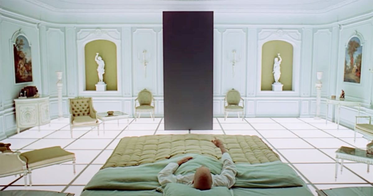 Elderly Dave Bowman lying in bed reaching toward the monolith in the neoclassical room in "2001: A Space Odyssey"