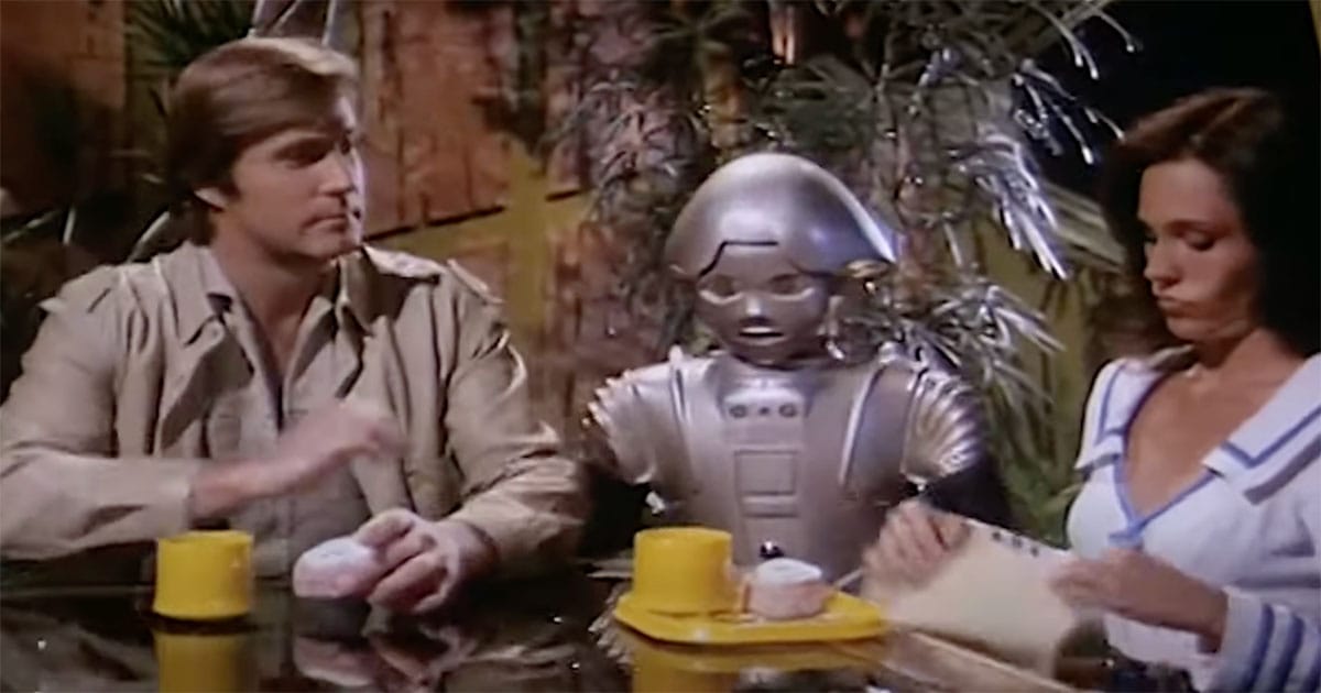 Buck Rogers, Twiki the robot, and Wilma Deering sitting at a futuristic café table with pastries and coffee.