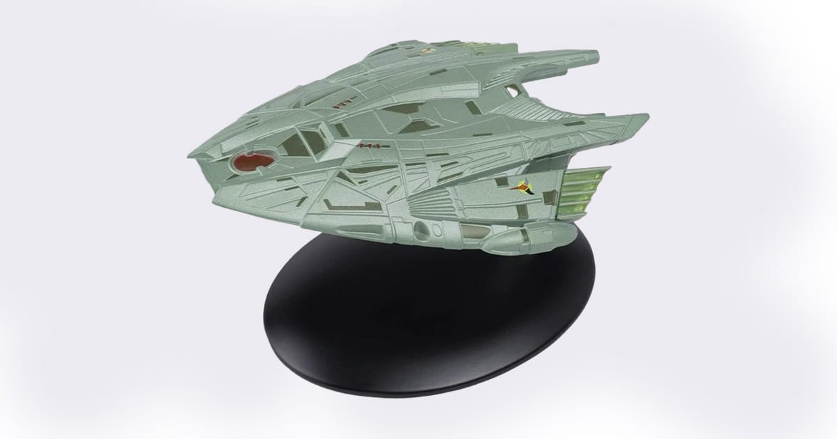 Model of the Klingon Transport starship from "Star Trek," featuring angular die-cast construction with green detailing, mounted on a black display stand.