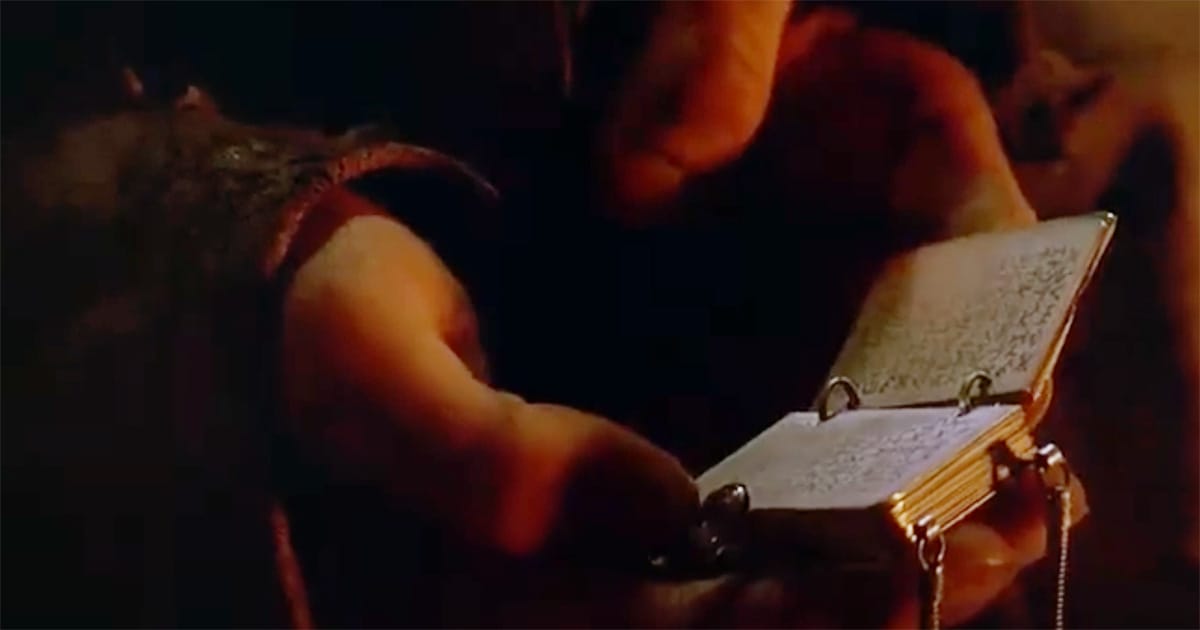 Close-up of the Drac lineage book held in Davidge’s hands in "Enemy Mine," representing Jeriba Shigan’s cultural legacy.
