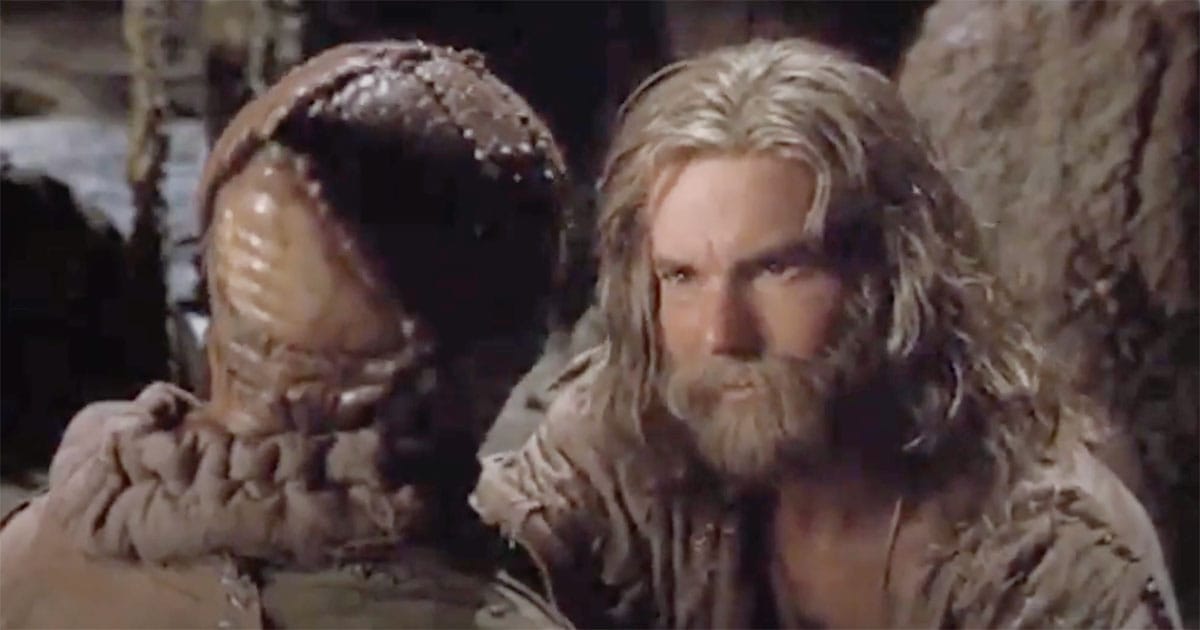 Davidge stares seriously at Zammis in a cave on Fyrine IV, reflecting the emotional weight of raising a child from an enemy species in "Enemy Mine."