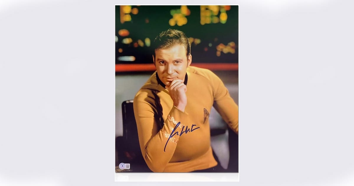 Autographed photo of William Shatner as Captain Kirk, seated in uniform with a thoughtful pose on the bridge of the USS Enterprise, featuring certified signature and authentication label.