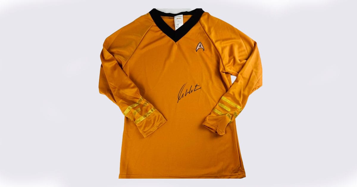 Gold Starfleet long-sleeve shirt signed by William Shatner, featuring black collar, rank stripes on sleeves, and the Star Trek insignia on the chest.