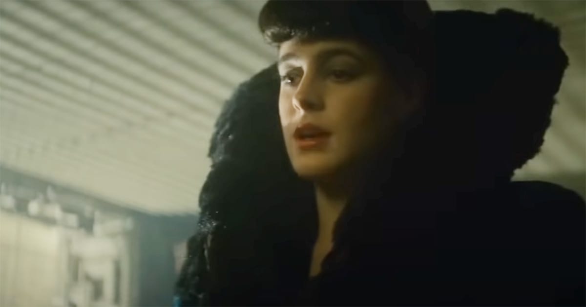 Rachel from Blade Runner in a dimly lit scene, wearing a dark coat with high collar, looking thoughtful.