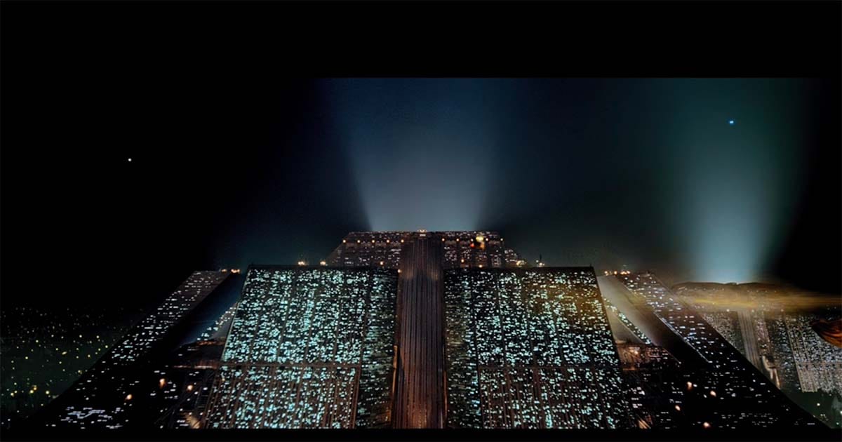 Massive futuristic pyramid building glowing at night above the dark cityscape with beams of light piercing the sky