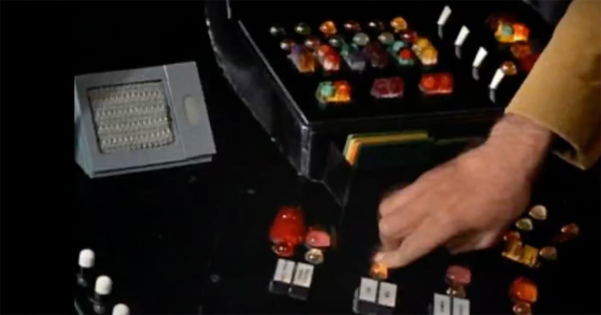 Close-up of a "Star Trek" control panel with colorful jelly bean buttons and a crew member’s hand adjusting controls on the Enterprise set.