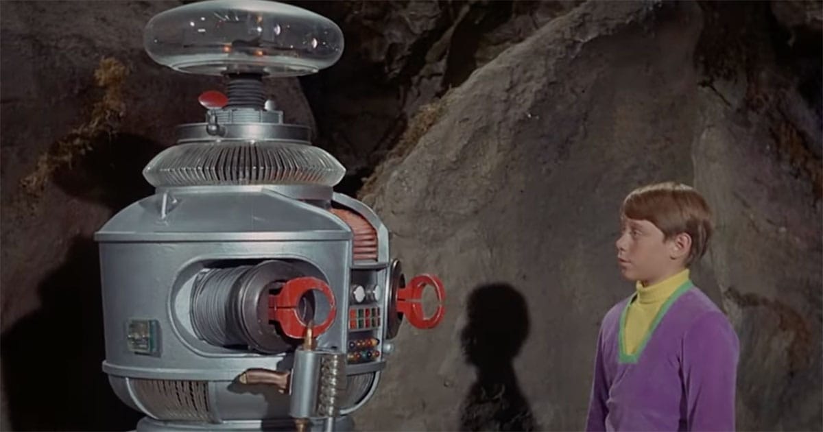 Will Robinson gazing at the Robot in a rocky alien cave in a scene from "Lost in Space," symbolizing trust between man and machine.