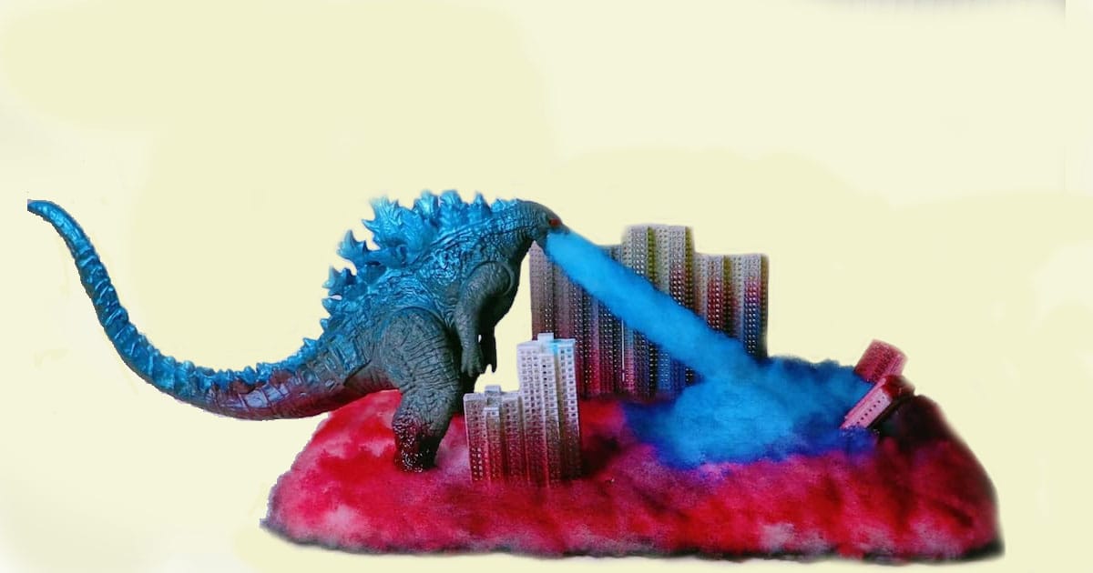 Godzilla figure emitting blue atomic breath at city buildings, surrounded by red and blue cotton-like smoke effects.