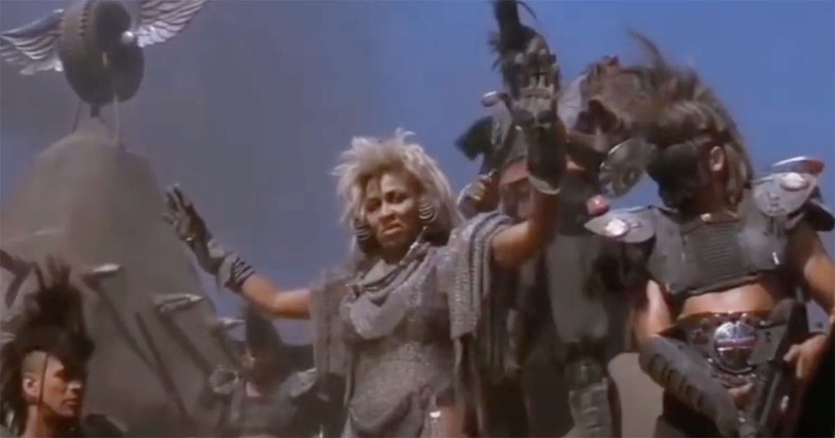 Tina Turner as Aunty Entity raising her arms in command, flanked by guards in Mad Max Beyond Thunderdome
