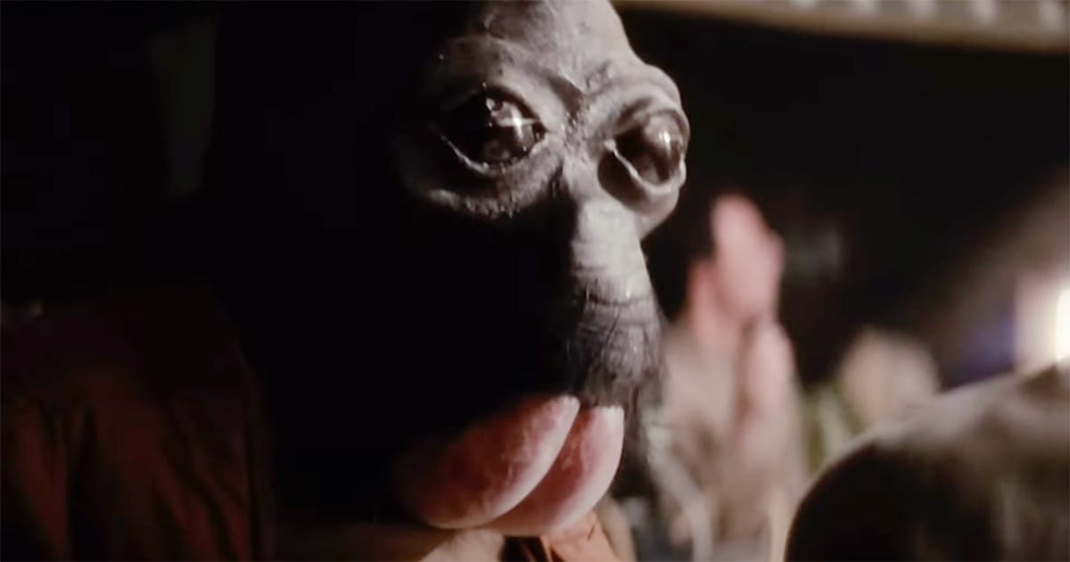 Close-up of a Roonan alien with a bulbous head and wide, glossy eyes seated in the Mos Eisley Cantina scene from "Star Wars: A New Hope."