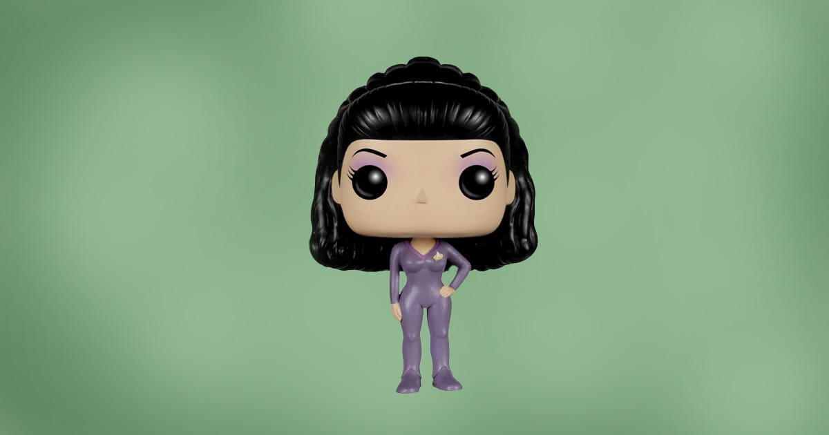 Funko Pop figure of Deanna Troi from Star Trek: The Next Generation wearing a purple jumpsuit, standing with one hand on hip, against green background.