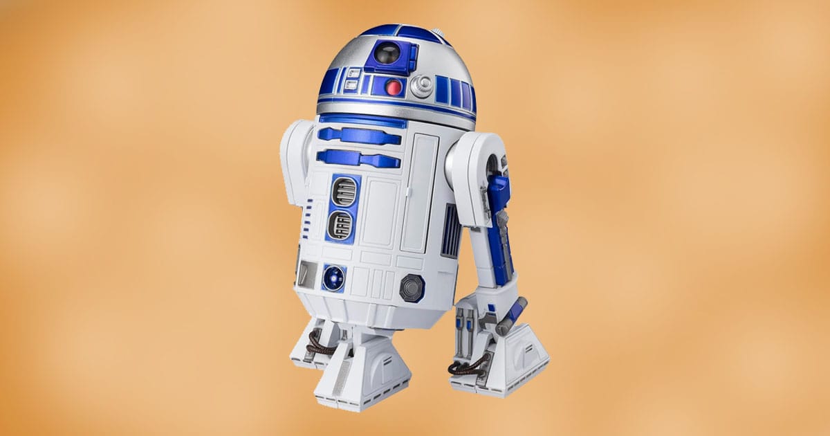 R2-D2 action figure with silver dome and blue detailing shown against a warm neutral background.