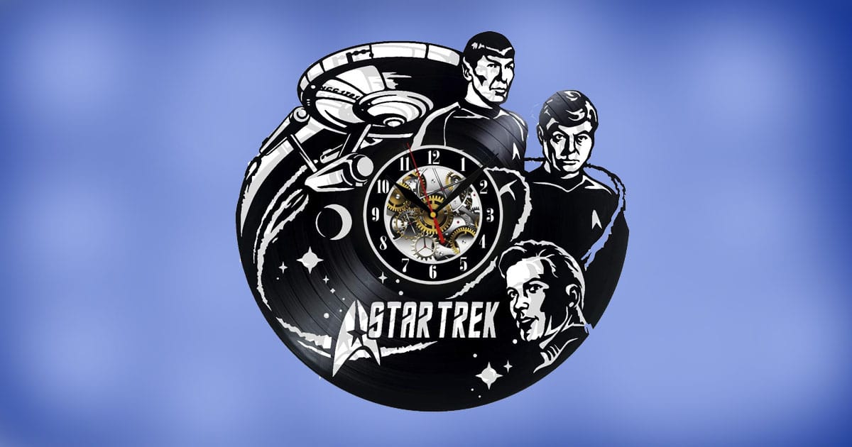 Star Trek vinyl wall clock featuring cutout designs of the Enterprise, Spock, Kirk, and McCoy with mechanical clock face on a blue background.