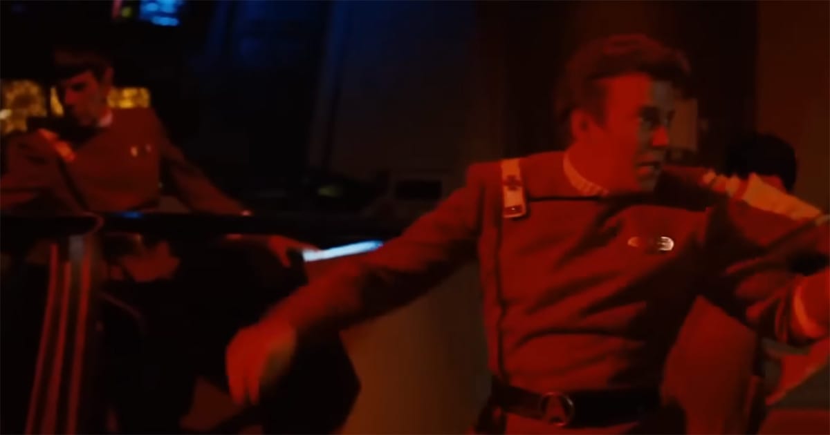 Kirk caught mid-struggle in red alert chaos as Spock braces behind him, the illusion of order giving way to urgency.
