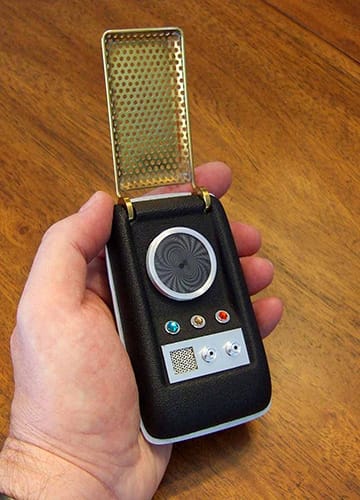 Close-up of a hand holding a replica of the Star Trek communicator, the flip-open device that inspired the look of Motorola flip phones.