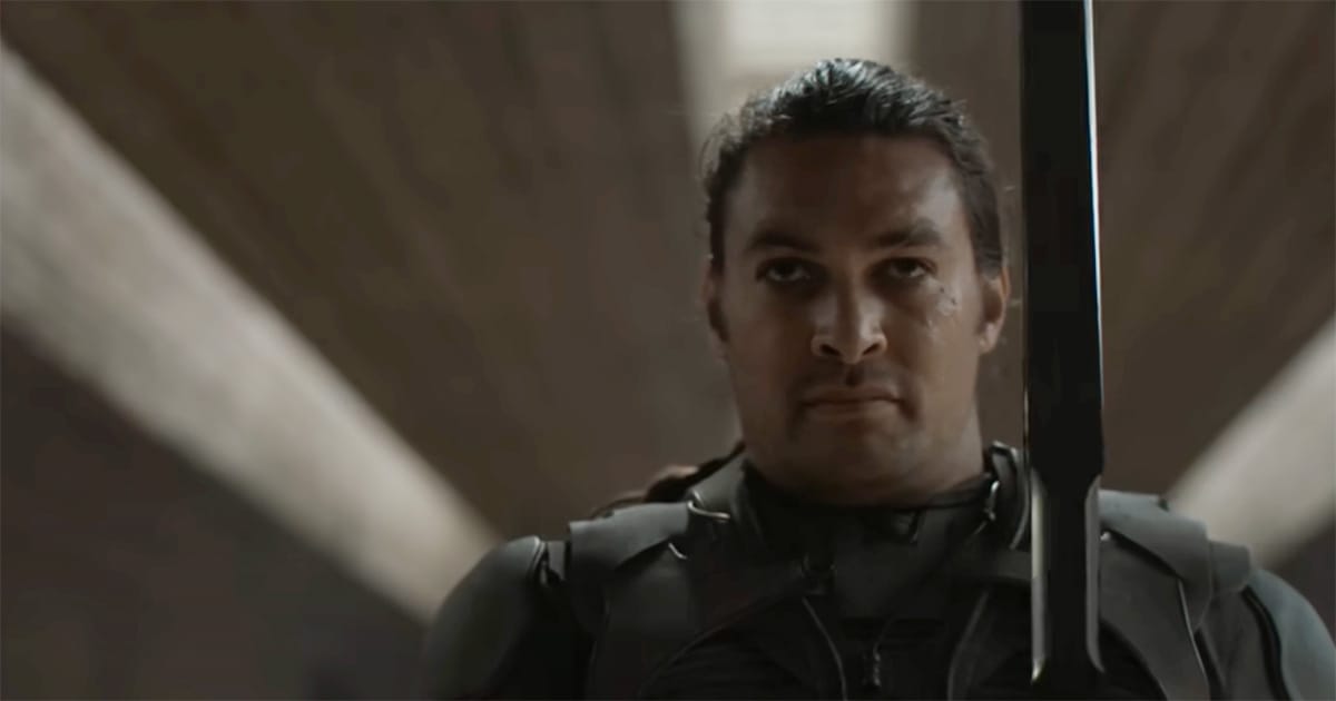 Duncan Idaho stands in Atreides armor, holding his blade upright with calm focus inside a sunlit stone corridor on Arrakis.