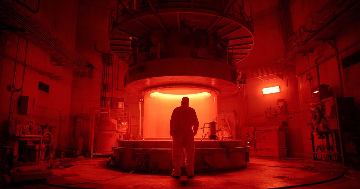 A scientist in a radiation suit stands in a glowing red reactor chamber.