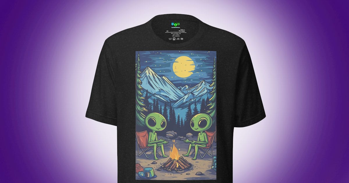 Two green aliens sitting by a campfire under a moonlit mountain sky on a black T-shirt.