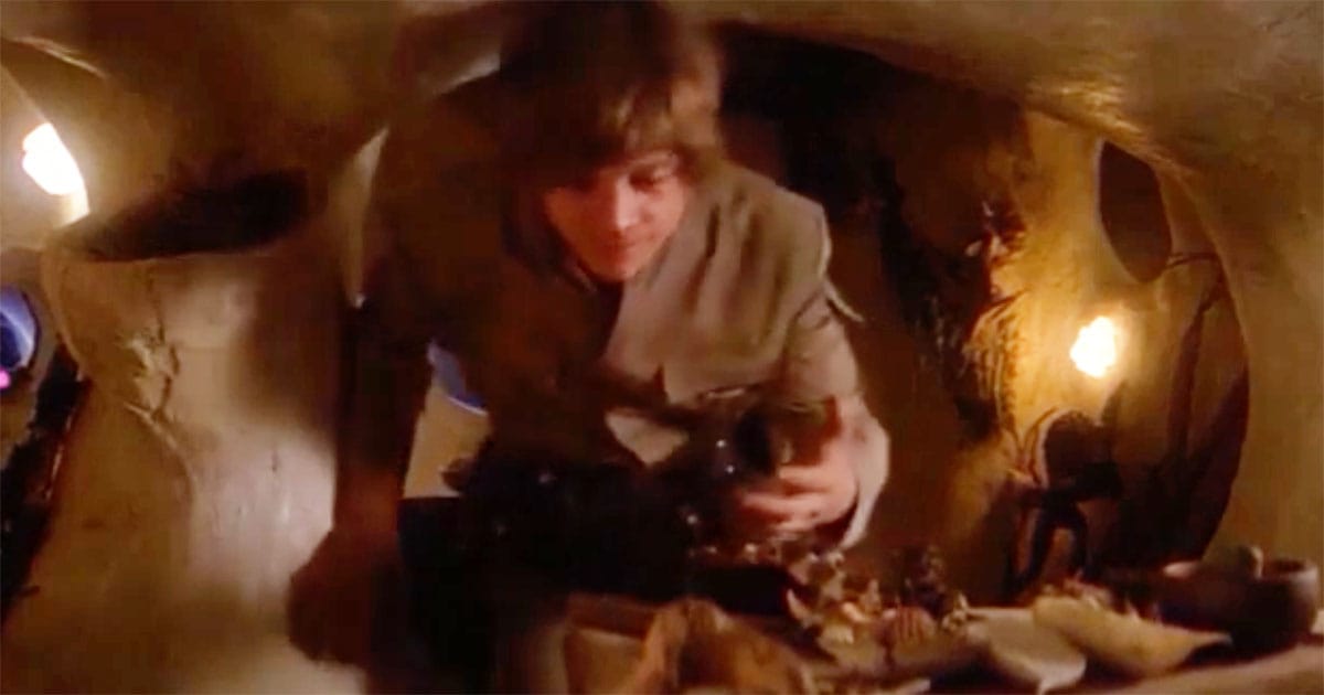 Mark Hamill as Luke Skywalker moving a red and cream striped snake aside to reach a bowl inside Yoda’s hut on the Dagobah set during The Empire Strikes Back filming