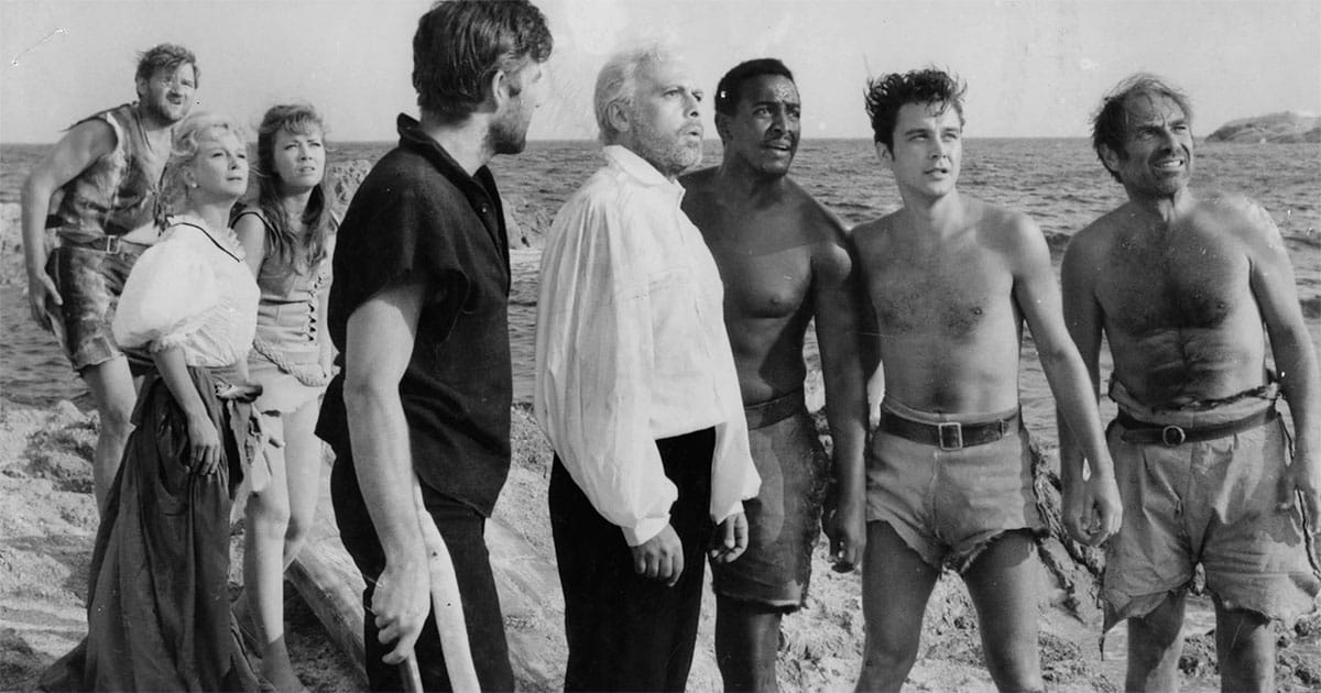 Six men and two women on a beach. Still image from the movie.