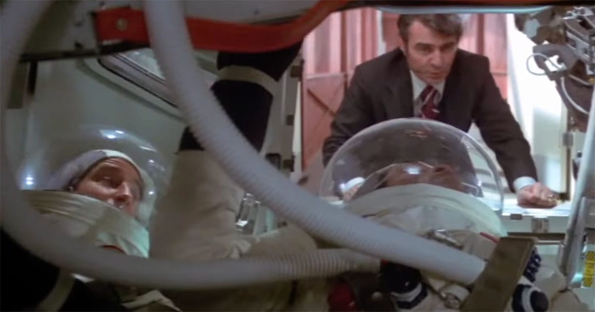 A government official speaking to astronauts inside a spacecraft capsule before launch in the 1977 film Capricorn One.