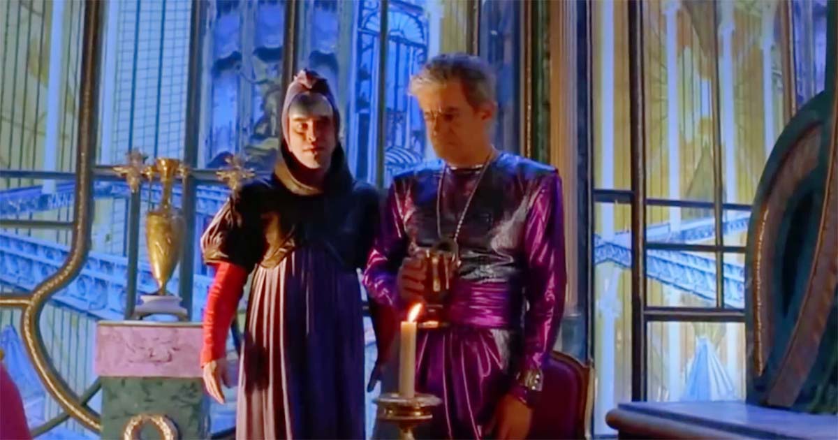 Count Hasimir Fenring standing beside Emperor Shaddam IV in an ornate imperial chamber, a candle burning between them as the Emperor looks away.