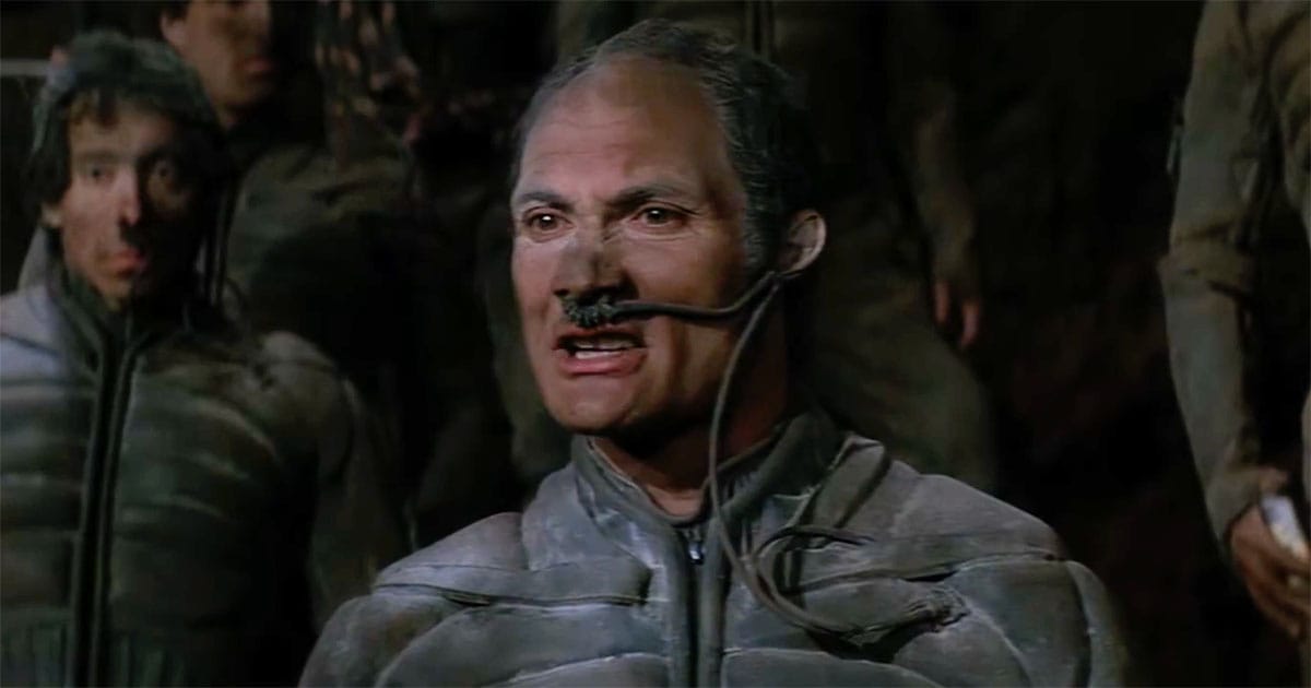 Jamis in the 1984 Dune film wearing a stillsuit with nasal tube inside a Fremen cavern.