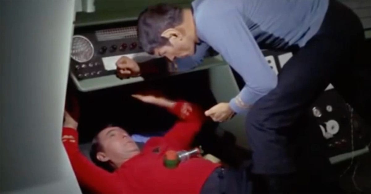 James Doohan as Scotty working beneath an engineering console while Mr Spock assists aboard the original Star Trek Enterprise.