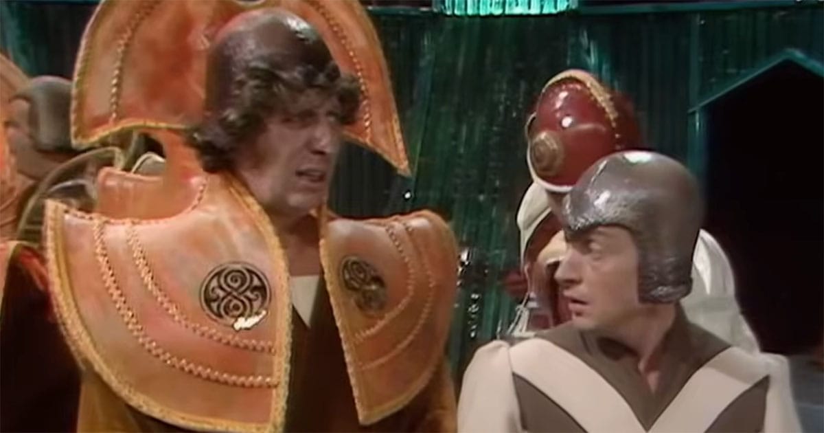 Time Lord in orange ceremonial collar speaking with another figure showing contrast with the Doctor in Doctor Who.