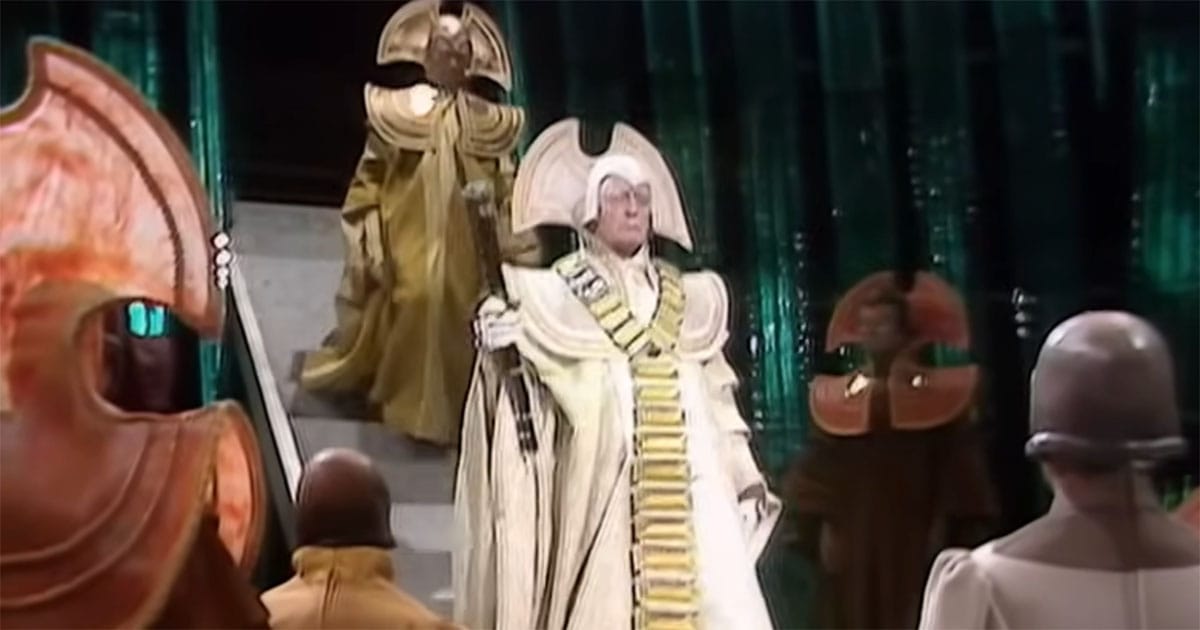 White-robed Time Lord leader with staff in ceremonial setting on Gallifrey in Doctor Who.