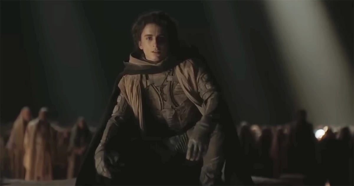 Paul Atreides standing before a gathered crowd in low light, symbolizing how prophecy and belief elevate him into a messianic figure in Dune.