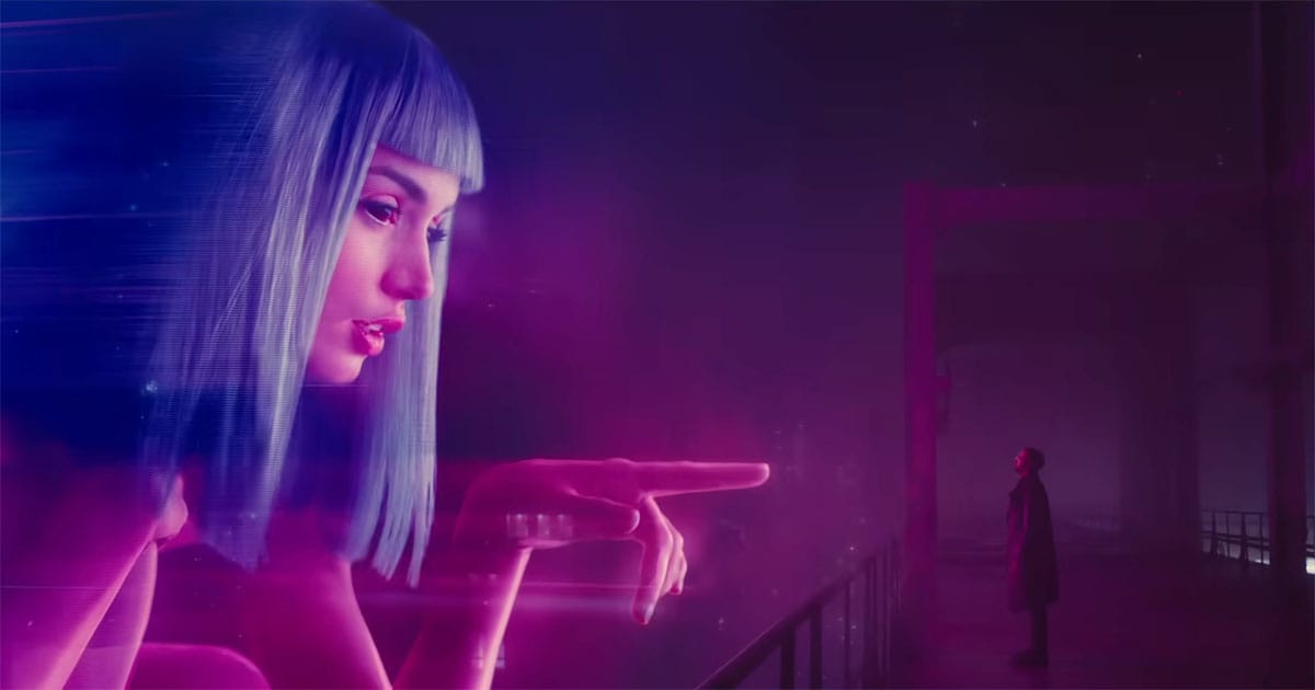 Officer K standing beneath a giant Joi hologram in “Blade Runner 2049” representing artificial humanity and emotional isolation.