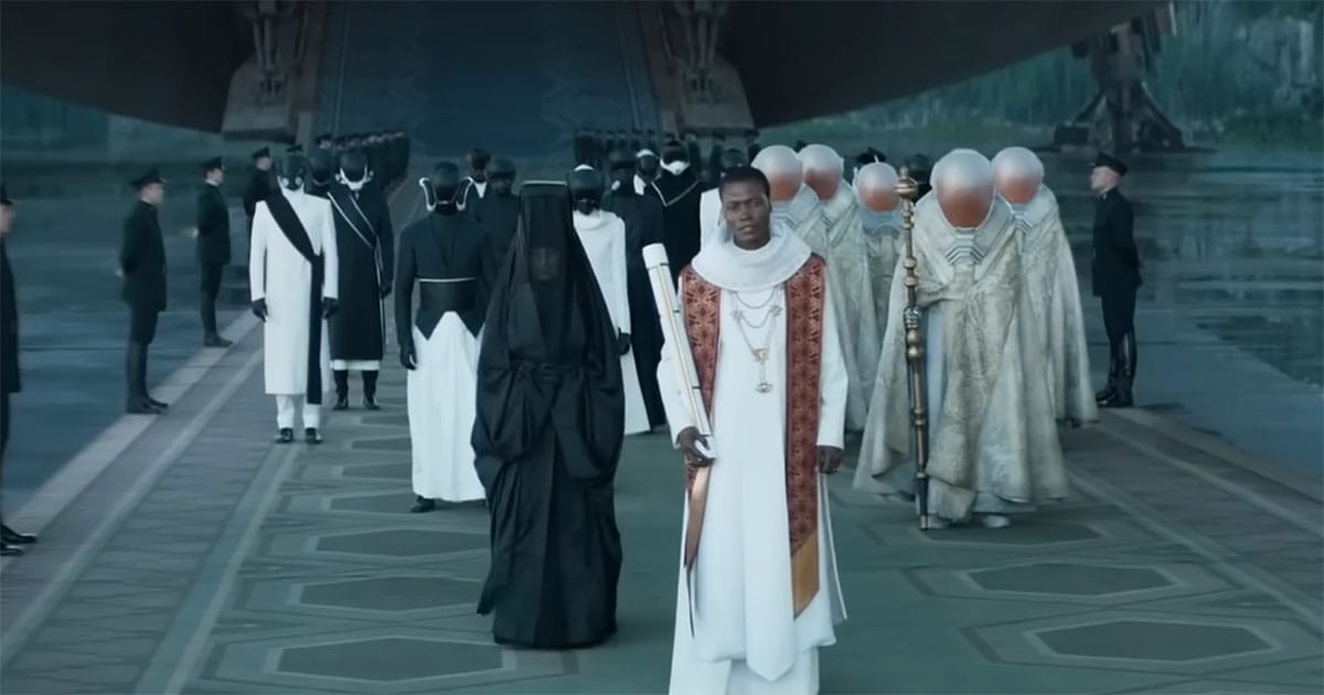 Members of the Imperial court walk in ceremonial formation while attendants and military personnel frame the scene in a vast formal setting.