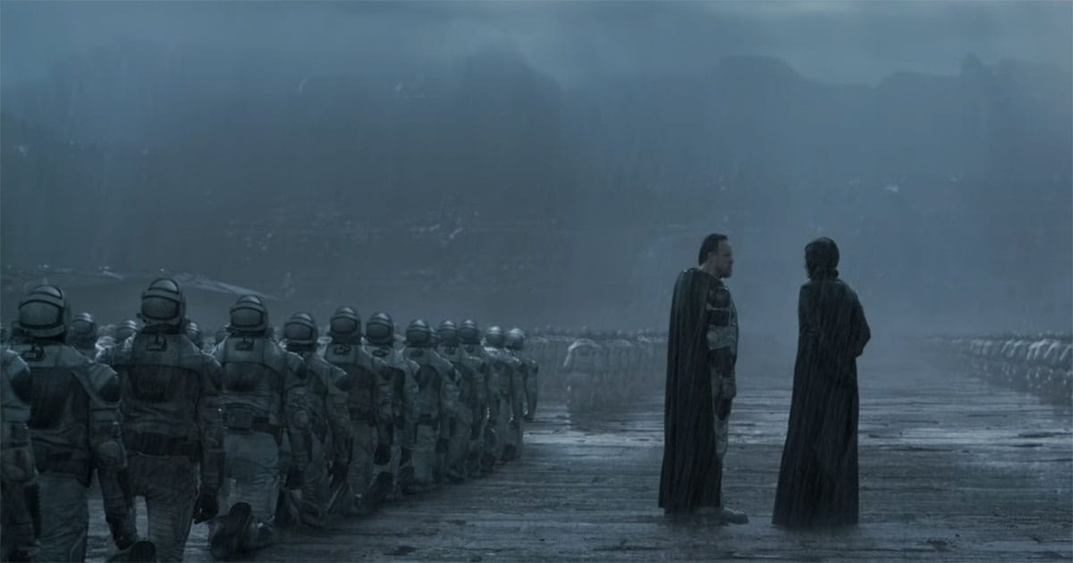Rows of Sardaukar kneel in formation while two Imperial figures stand at the center beneath rain and a dark sky.