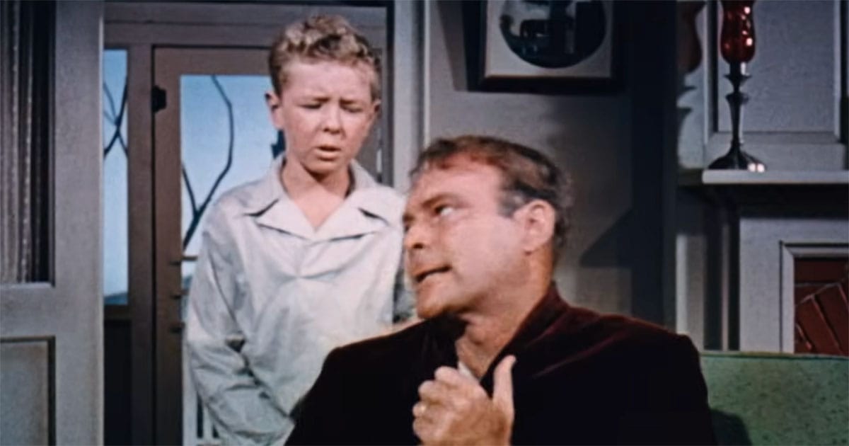 Scene from "Invaders from Mars" showing a young boy watching his father behave strangely inside their home, conveying fear and tension within the family.