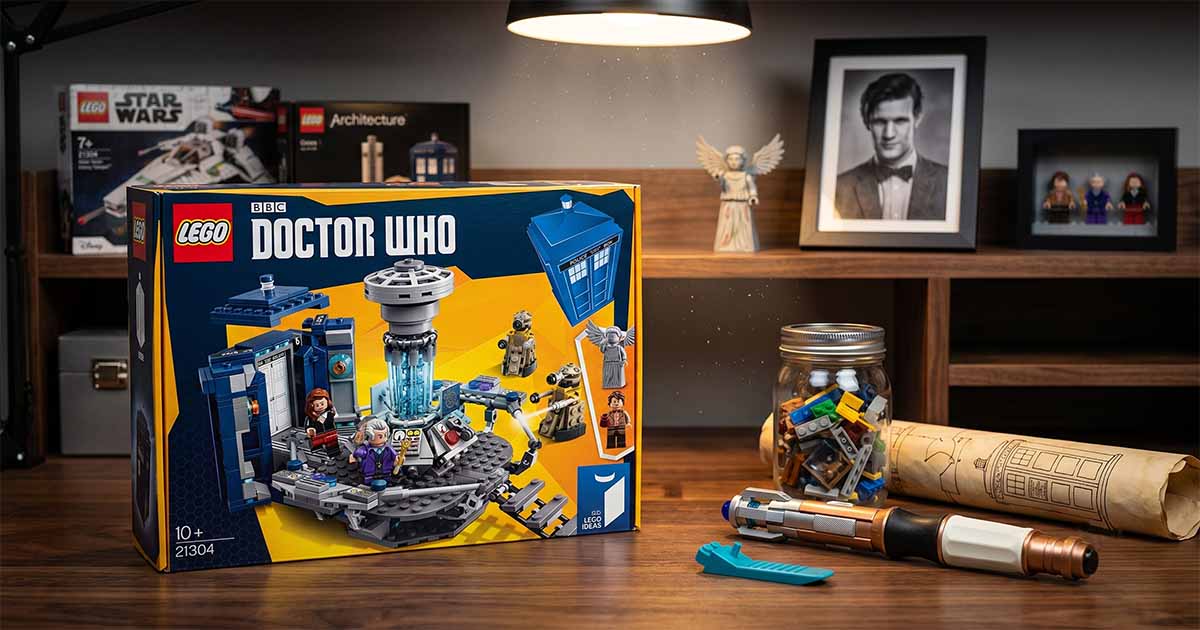 LEGO Ideas Doctor Who TARDIS building set displayed on a desk with a sonic screwdriver prop, Weeping Angel figure, and Eleventh Doctor photograph in the background.