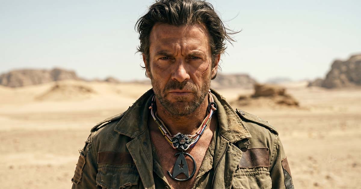 Portrait of a rugged man in a desert wearing a weathered science fiction necklace inspired by Khan with exposed wires, metal components, and a large pendant.