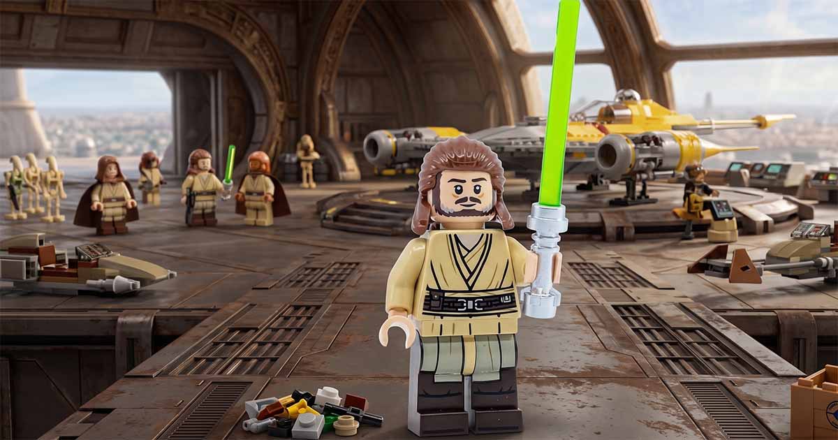 LEGO "Star Wars" Qui-Gon Jinn minifigure holding a green lightsaber inside a Jedi hangar with starfighters in the background.