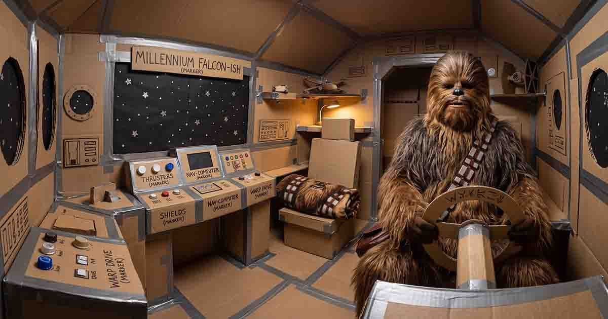 Chewbacca costume inside a homemade Millennium Falcon cockpit with cardboard controls and a pilot’s chair.