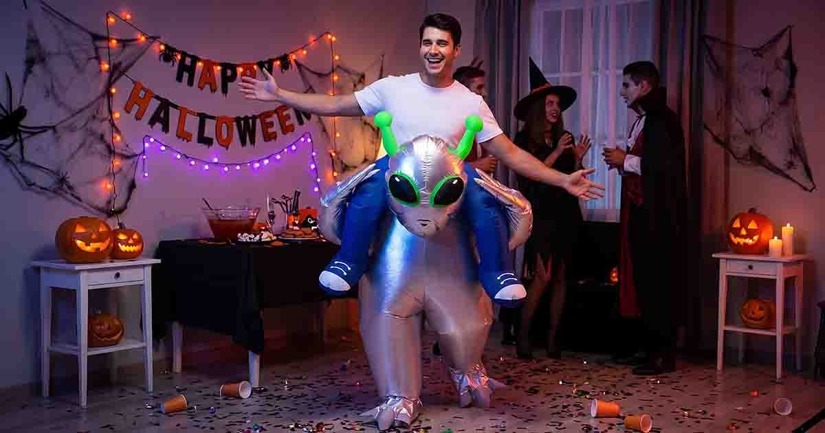 Man wearing an inflatable alien abduction costume at a Halloween party with pumpkins and costumed guests.