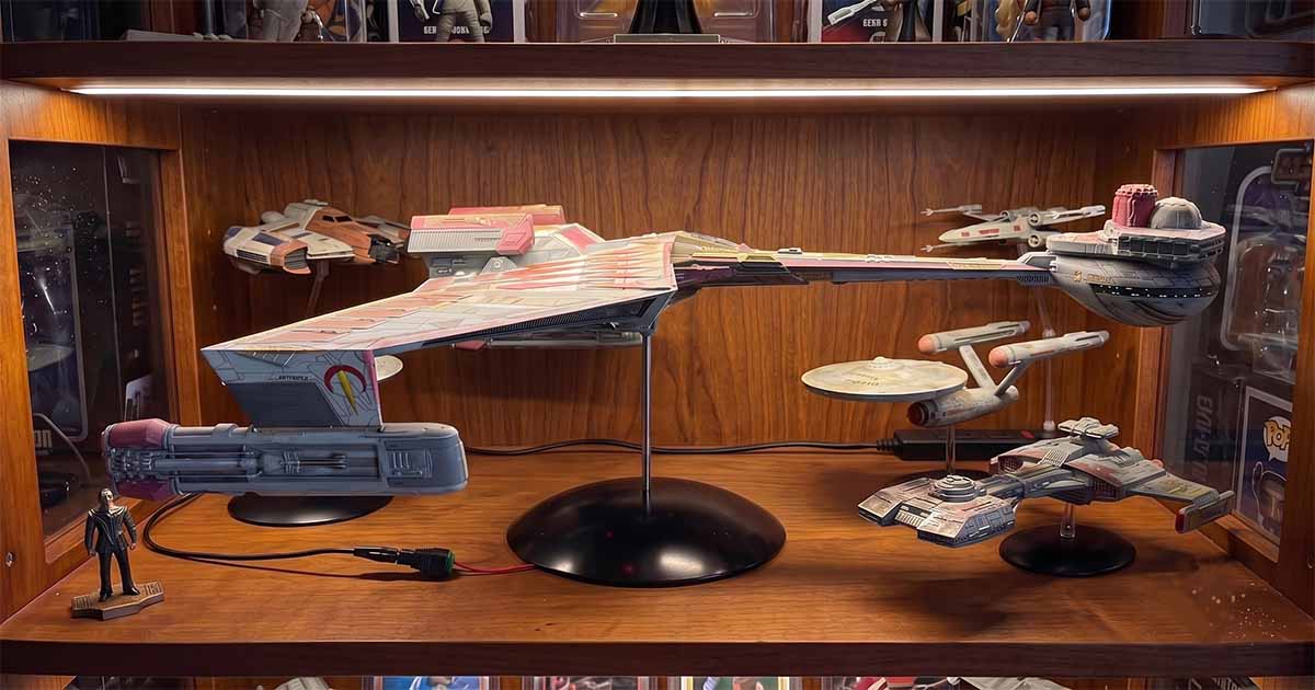 Klingon Kronos One model displayed on a black stand inside a wooden collector cabinet with several Federation starship models and character figures.