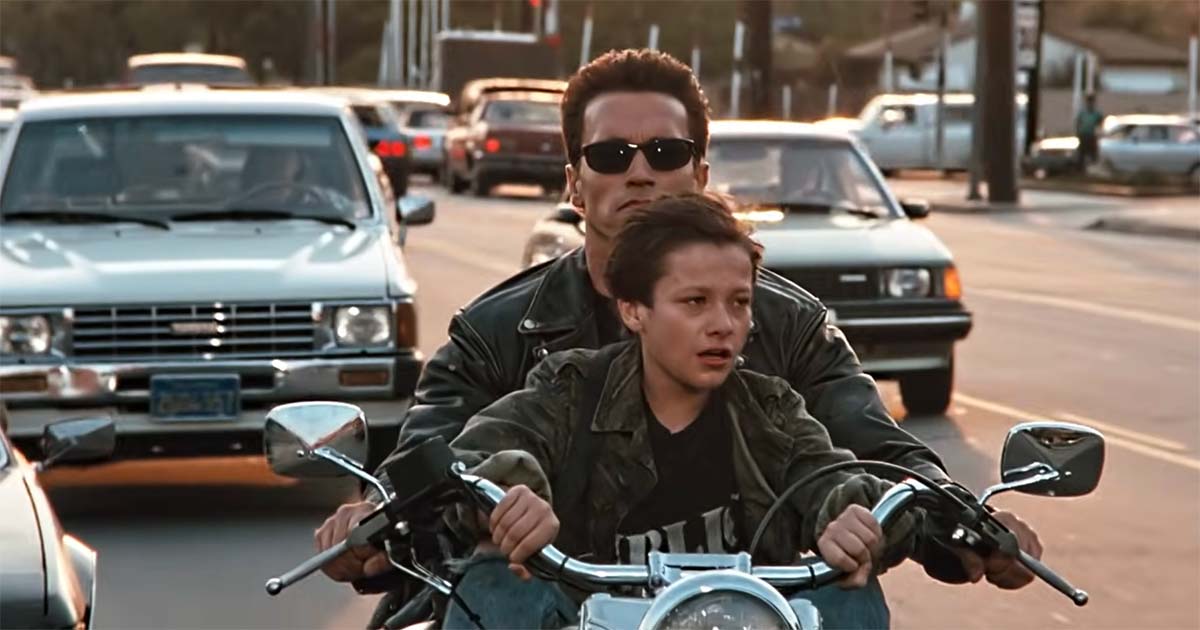 John Connor rides in front of the T-800 on a motorcycle.