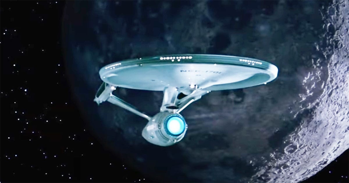 The USS Enterprise flies above the surface of a distant world against a field of stars.