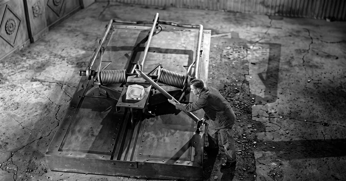 A tiny Scott Carey uses a long pole to disarm an enormous mousetrap baited with cheese in “The Incredible Shrinking Man.”