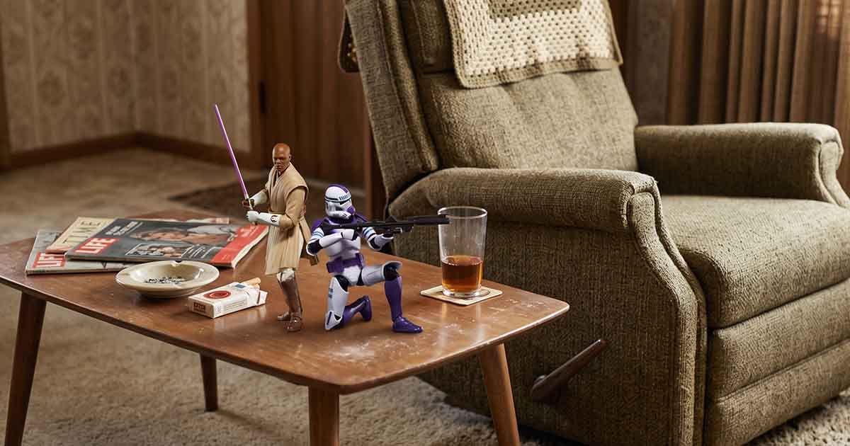 Mace Windu and a 187th Legion clone trooper action figure posed on a vintage coffee table beside magazines, a drink, and an armchair.