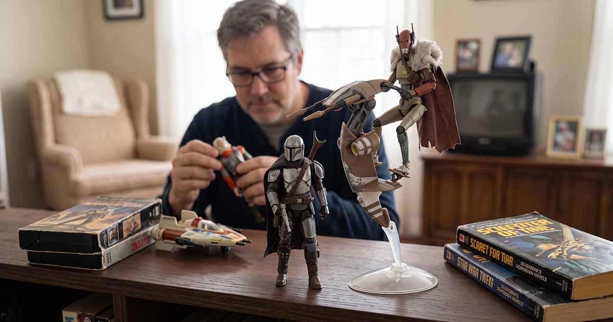 The Mandalorian action figure posed beside a mercenary guard droid and speeder bike on a table with vintage science fiction books and toys.
