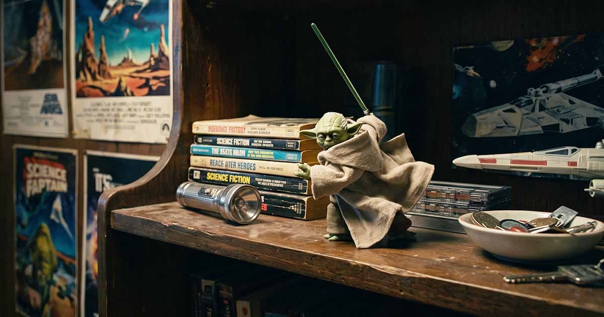 Yoda action figure holding a green lightsaber on a shelf surrounded by vintage science fiction books, toys, and memorabilia.