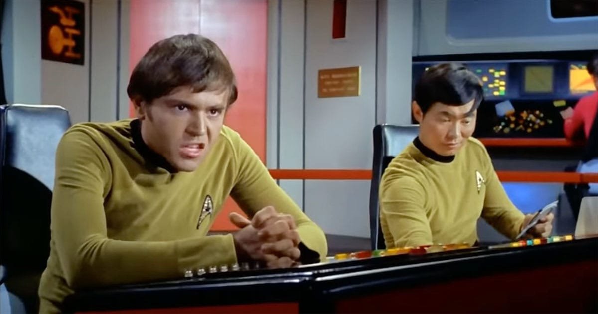 Chekov leans forward with clasped hands beside Sulu at their stations on the Enterprise bridge in “Star Trek.”
