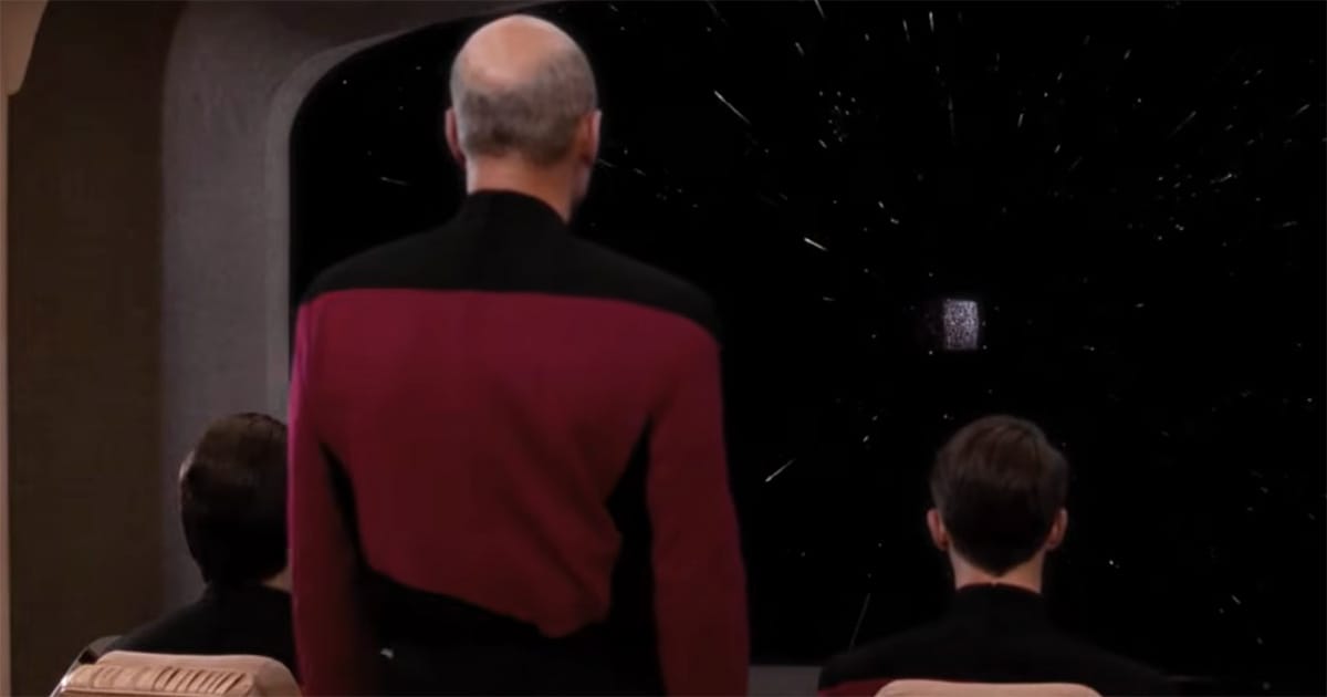 Jean-Luc Picard stands on the Enterprise bridge facing a starfield on the main viewscreen.